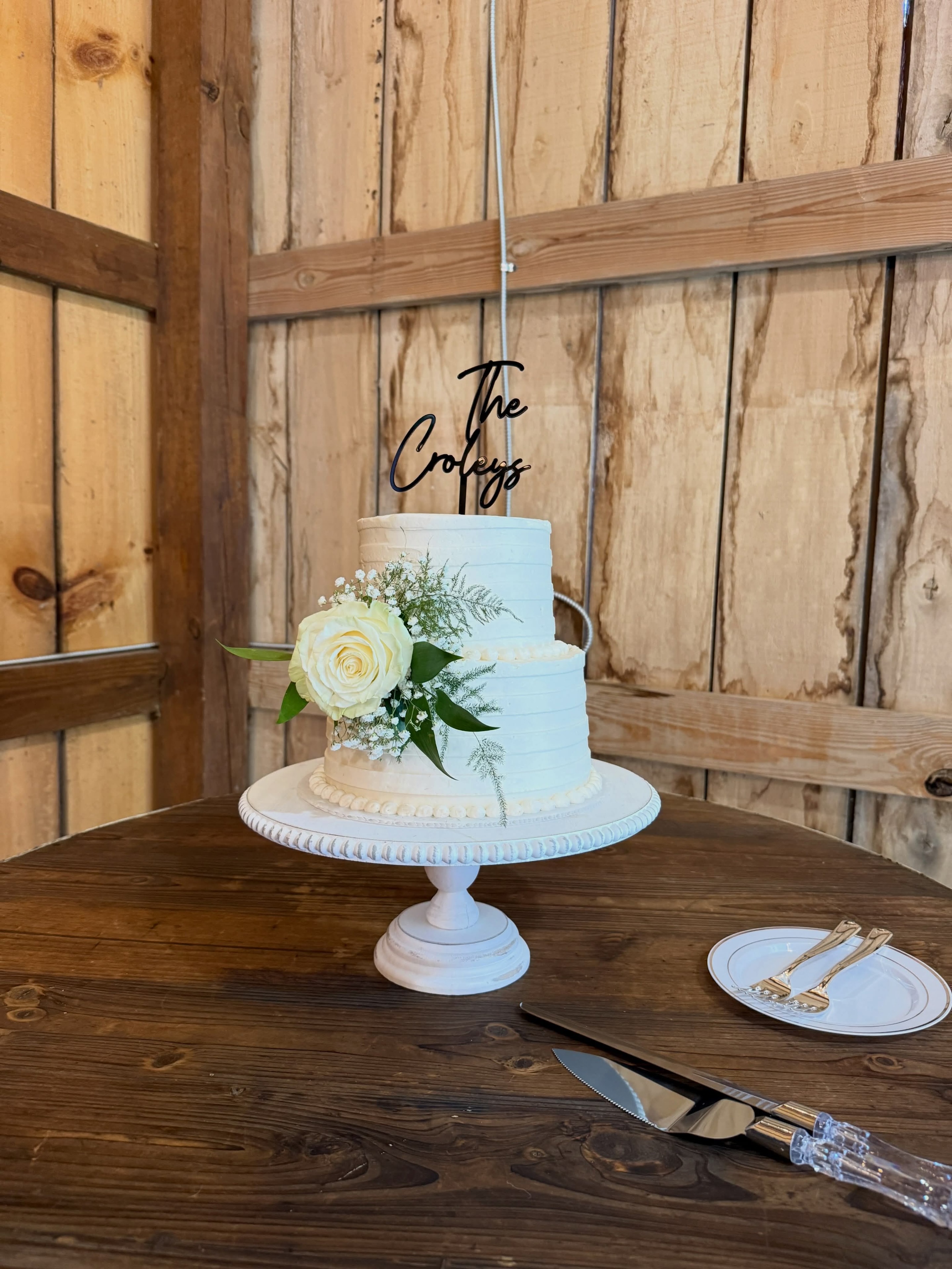 White wedding cake with rose topper in a rustic barn setting